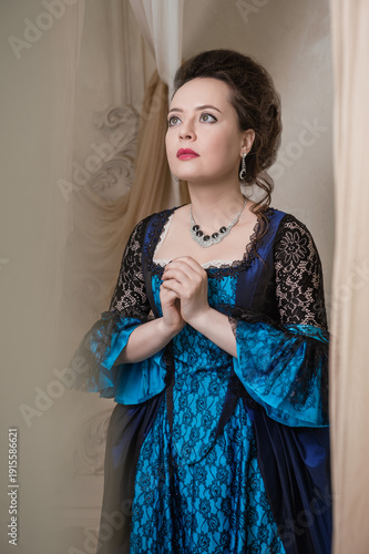 Konstfotografi Beautiful woman wearing blue medieval dress praying stands among ancient ruin