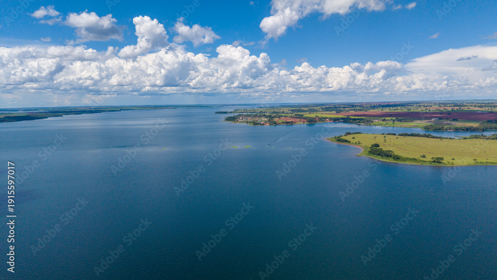Fototapeta premium A serene aerial view of a vast body of water surrounded by lush green land and a vibrant blue sky