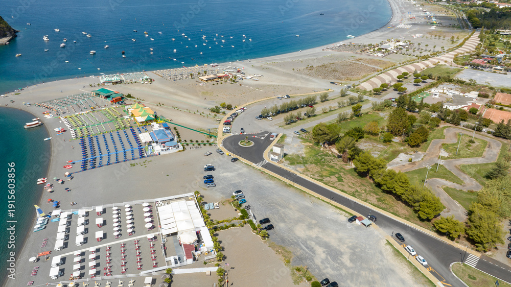 Fototapeta premium Aerial view of Praia a Mare beach, located in the province of Cosenza, Calabria, southern Italy. There are many beach resorts along the coast overlooking the Tyrrhenian Sea. Summer sunny morning.