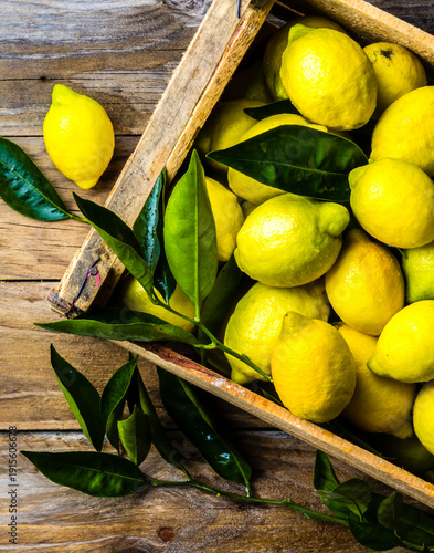Box of lemons with fresh leaves on wooden background with copy space. Top view