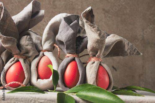 Easter table setting with decorated eggs wrapped as bunnies on a grey cloth background 