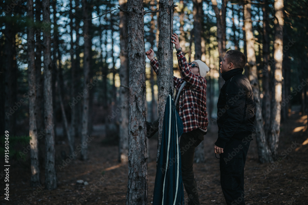Fototapeta premium Two people in a forest work together to set up a tent, capturing a calm outdoor moment.