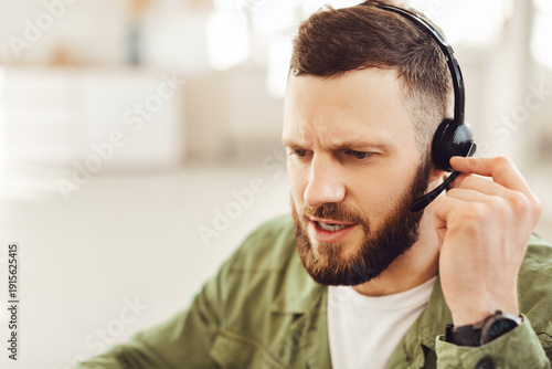 фотографія Side View Portrait Of Male Hotline Operator Wearing Headset Making Video Call Talking And Communicating With Customers Indoors