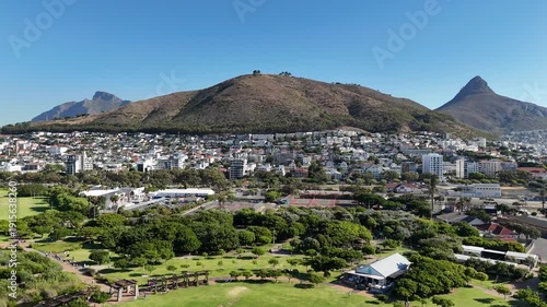 Drone lowers over Green Point Park with view of Devil's Peak, Table Mountain, Signal Hill, and Lion's Head on sunny day in Cape Town, South Africa