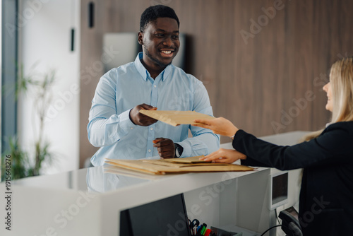 Fényképezés Courier delivering padded envelope to woman at reception desk