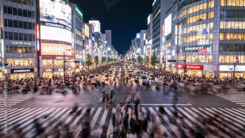 Busy city street intersection with large crowd gathered at night surrounded by tall buildings and neon advertisements.