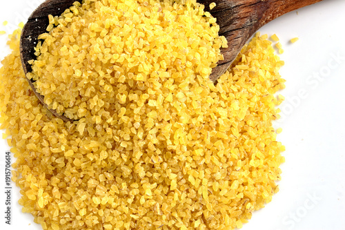 Yellow couscous, ready to cook, sits in a wooden spoon.