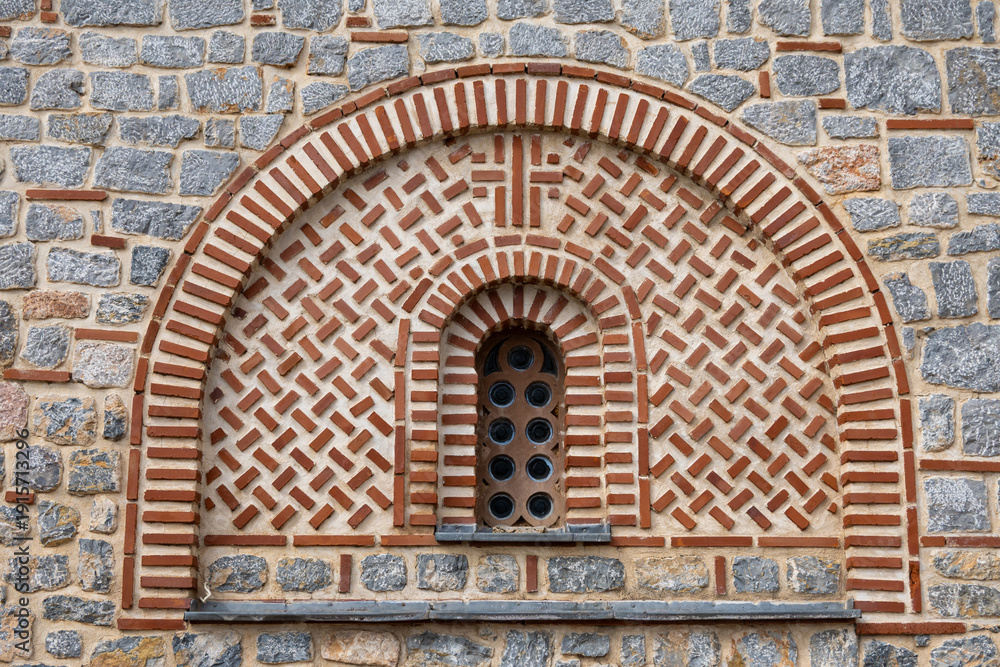 Obraz premium An architectural window, featuring a semicircular arch and small circular panes, set within decorative brick and stone masonry patterns at Church of Saints Clement of Ohrid and Panteleimon.
