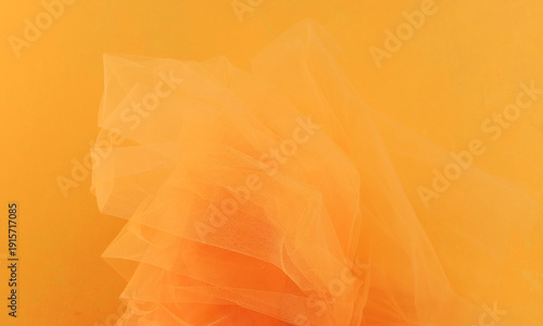 Bright orange yellow tulle fabric on yellow background.  Abstract transparent material curve wave.
