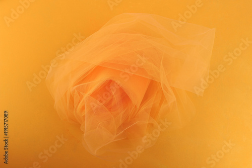 Bright orange yellow tulle fabric on yellow background.  Abstract transparent material curve wave.