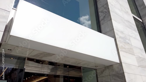 Modern building facade with white marble cladding and a prominent white overhang above the entrance reflecting a blue sky and white cloud