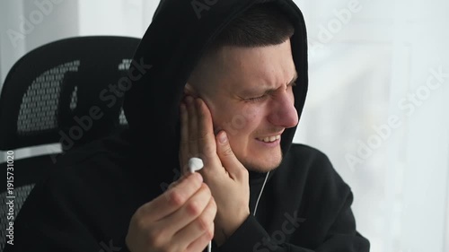 A man removes headphones from his ears due to severe pain.
Listening to loud music on headphones
