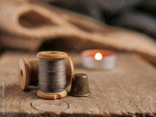 Vintage wooden thread spool and antique metal thimble on a rustic wood block. A high-quality still-life photograph capturing traditional sewing tools and textures, ideal for tailoring, handicraft blog