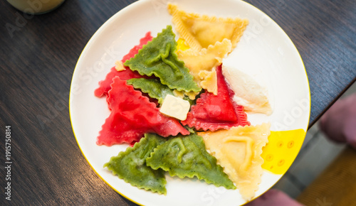 Plate of colorful ravioli with butter on a dark wooden table close-up. Delicious traditional Italian pasta meal. Culinary photography.