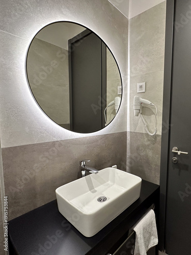 Modern bathroom with round mirror and stylish sink in contemporary hotel. Cleanliness, comfort, hygiene, and modern minimalist interior design.