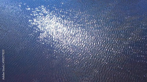 Reflection glares of the sun and clouds in the ripple water of the river brook. Slowly moving water grass weeds in the water. Top view of fantasy dreamy water in the North American wilderness.