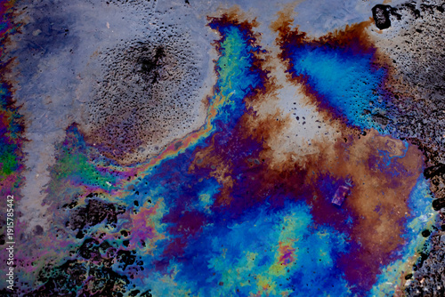 Colorful oil spill on wet asphalt surface creating abstract rainbow patterns. Environmental pollution concept with iridescent fuel slick texture
