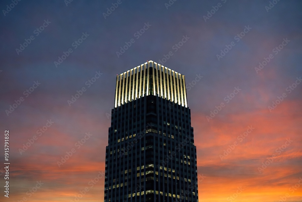 Obraz premium A modern skyscraper's illuminated crown against a dramatic sunset sky