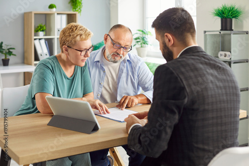 Senior couple sits with advisor reviewing and signing a contract and related document, formalizing agreement during a private meeting at desk. Elderly people make deal with agent in office.