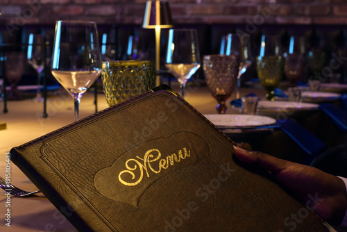 Tableau sur toile Closeup hand holding leather bound menu while seated at elegantly set restaurant table