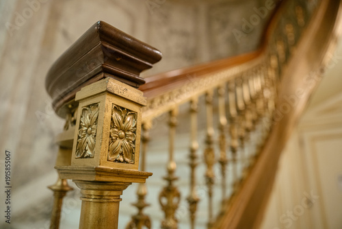 Fényképezés A close-up view of a staircase railing shows a golden floral carving and a dark polished wooden handrail