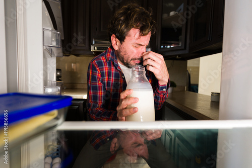 Fotografía Man reacting to bad smell from spoiled milk in fridge, pinching his nose with di