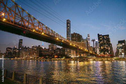 Bild auf Leinwand The Queensboro Bridge glows with lights as it spans across the East River, framing the New York City skyline at twilight