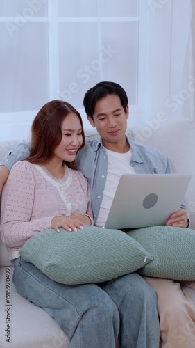 Happy asian couple video call on laptop together in living room at home, man and woman talking online cyberspace at home, technology connection and social media interaction, relationship and bonding.
