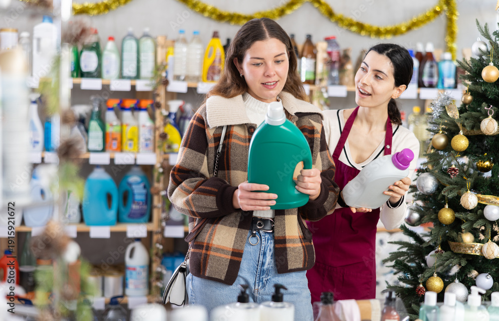 Obraz premium In X mas atmosphere, girl consultant helps female buyer choose laundry softener, answers questions and accompanies during shopping, recommended some item. .