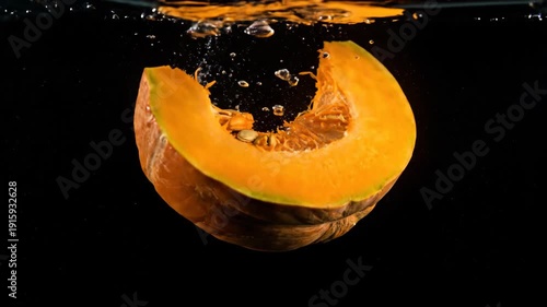 Fresh pumpkin slice falling into water on black backdrop, orange fruit, food.