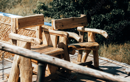 Romantic pair of rustic wooden chairs on a sunny deck, symbolic of togetherness and love in a peaceful garden, handcrafted outdoor seats for couples sharing a moment in a cozy vacation resort.