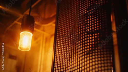 Pendant light casting warm illumination and creating a golden glow on an abstract metal mesh texture, emphasizing detail and industrial interior atmosphere with bokeh