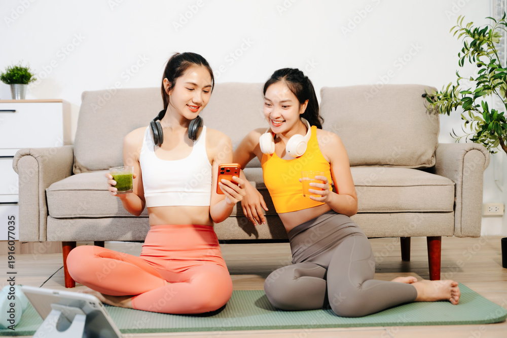 Obraz premium Two women enjoying home workout on yoga mat with headphones and mobile devices. Healthy lifestyle, fitness, wellness