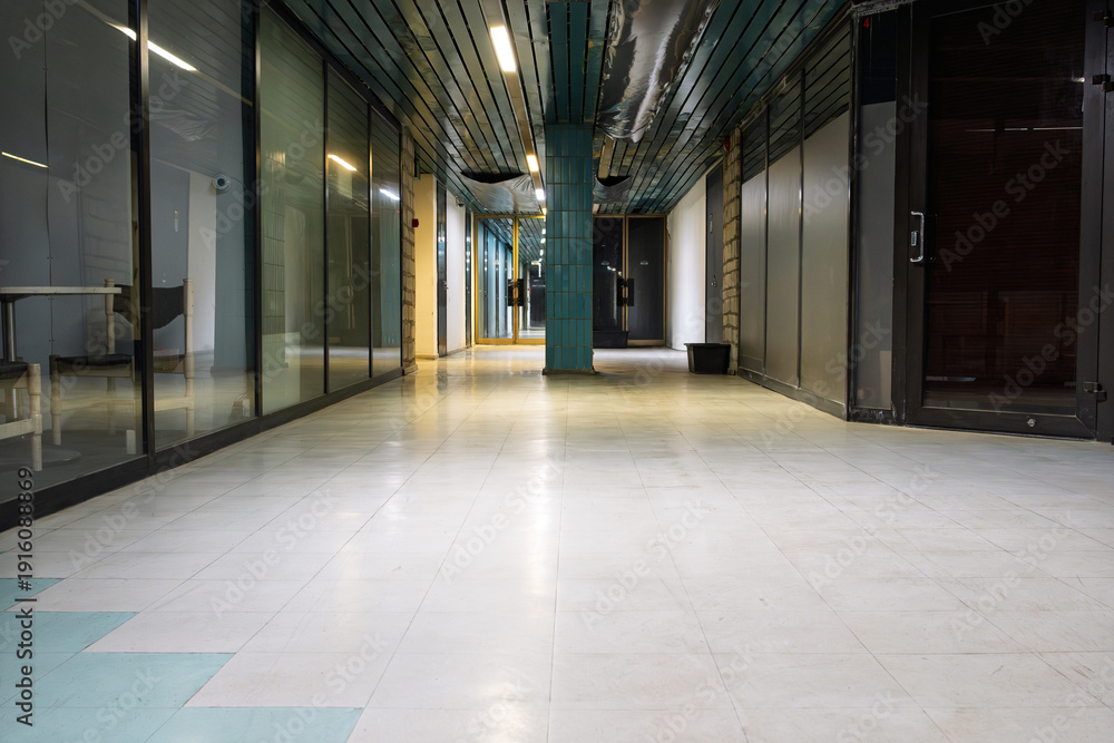 Obraz premium Empty Abandoned City Hall Building Corridor With Long Hallway, Glass Partition Walls, Teal Ceiling Panels, White Tiled Floor, And Atmospheric Fluorescent Lighting In A Vacant Historic Civic Space