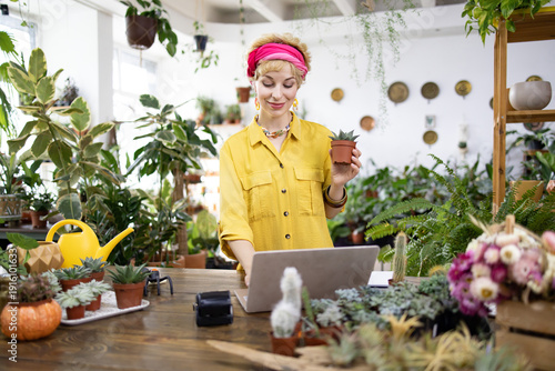 Schilderij op canvas A woman holds a small potted succulent while working on her laptop in a plant sh