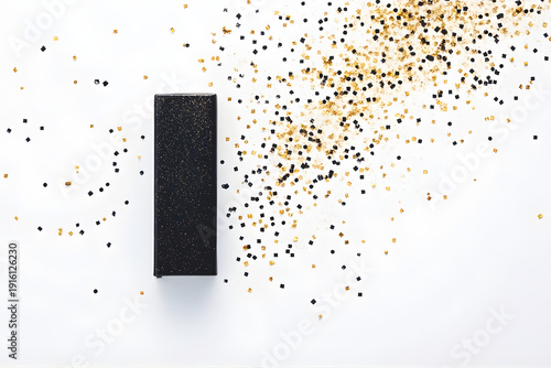 Black gift box with golden confetti on white background. Flat lay, top view. A rectangular black gift box with a subtle sparkle finish is placed on a white surface.
