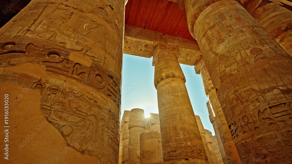 Fototapeta premium Ancient stone columns with carved hieroglyphs viewed from below inside Karnak Temple in Luxor Egypt under clear blue sky and warm sunlight