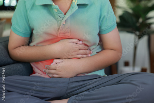 Obraz na plátně Asian boy holding belly suffering from severe abdominal pain with red inflamed area