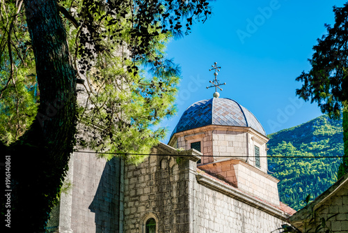 Wallpaper Mural Orthodox church in Risan town, Kotor bay, Montenegro. The building features a stone facade and a dome, surrounded by lush greenery and mountains in the background. Torontodigital.ca