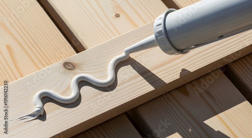 Silicone sealant tube dispensing bead onto wooden planks