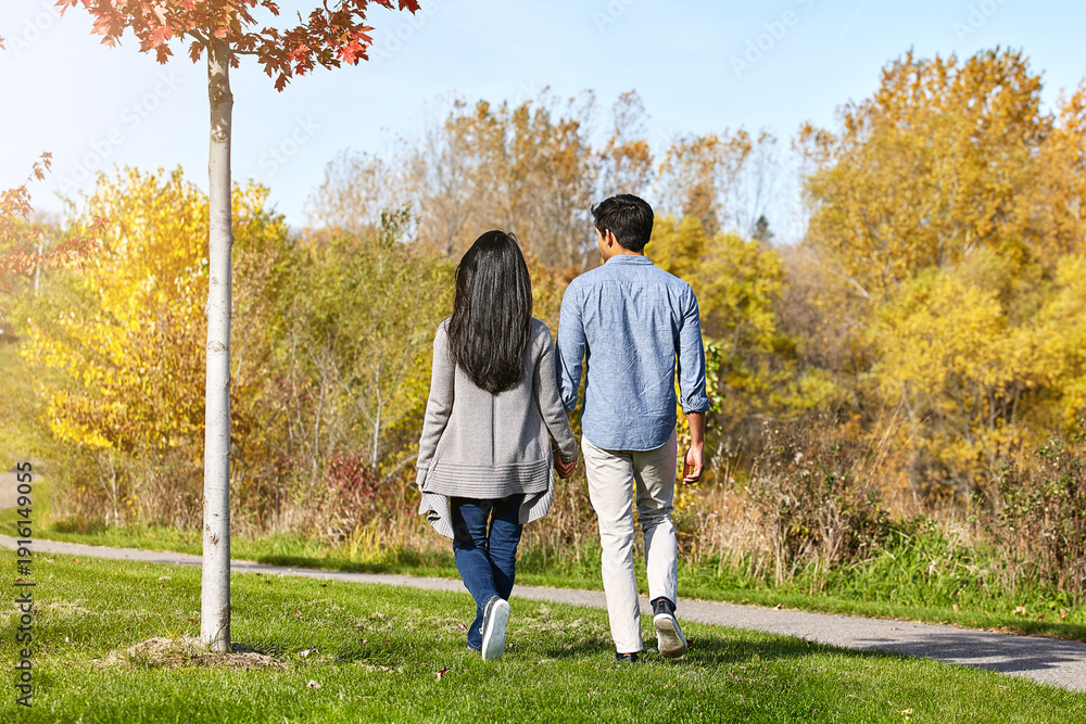 Fototapeta premium Holding hands, walking and back of couple in nature with love, care or bonding on vacation. Outdoor, travel and man with woman in park for connection together on holiday or weekend trip in Autumn.