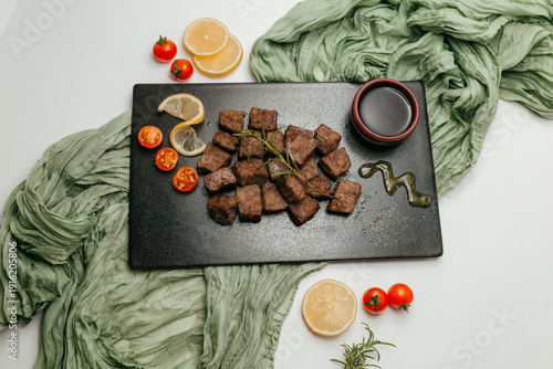Fried meat cubes served on black board with lemon and herbs