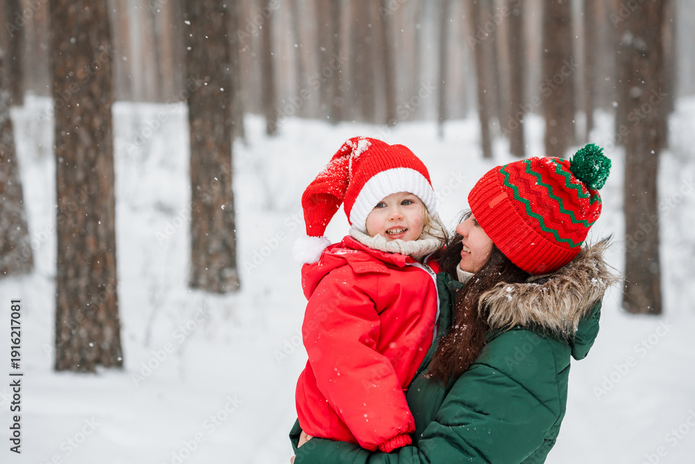 Fototapeta premium Little child girl in hat and winter jumpsuit with her mother outdoor in snow, family