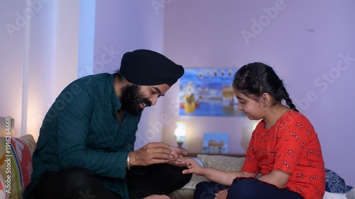 Indian father applying nail paint on her daughter's nails - cosmetic  father-daughter bonding. A North Indian Sardar in casual clothes is putting nail polish on his little girl's nails in the bedro...