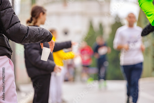 Volunteer offers a plastic cup of water to marathon runners