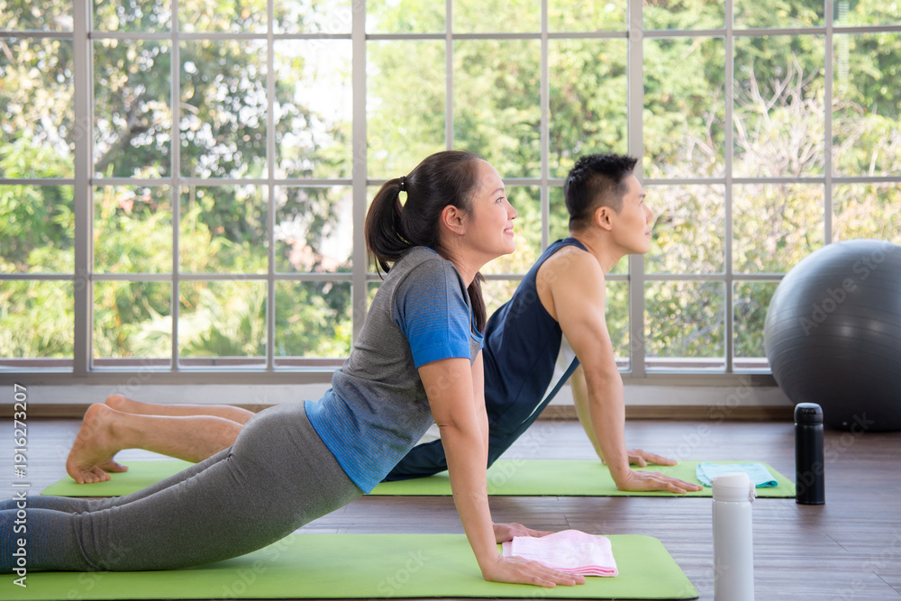 Obraz premium Happy smiling man and woman meditating in yoga at home. Asian active couple doing yoga pilates workout together in living room at home. Fitness. People and healthy lifestyle concept.