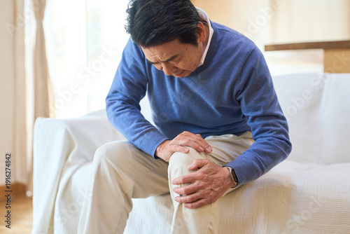痛む膝を押さえるアジア人シニア男性