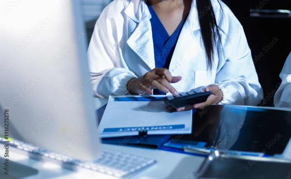 Fototapeta premium Medical team having a meeting with doctors in white lab coats and surgical scrubs seated at a table discussing a patients working online using computers in the medical industry.
