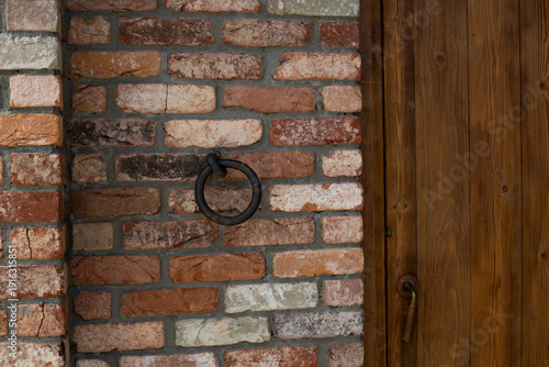 Iron doorknob for knocking on old house. Medieval door and knocker. Entrance to an ancient wooden door with vintage feel. Antique door in brick wall. Old metal brass knocker for door