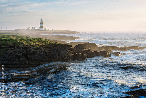 Quadro em tela Winter view of Hook Head lighthouse with crashing waves, green clifftops, and foaming Atlantic surf, Ireland
